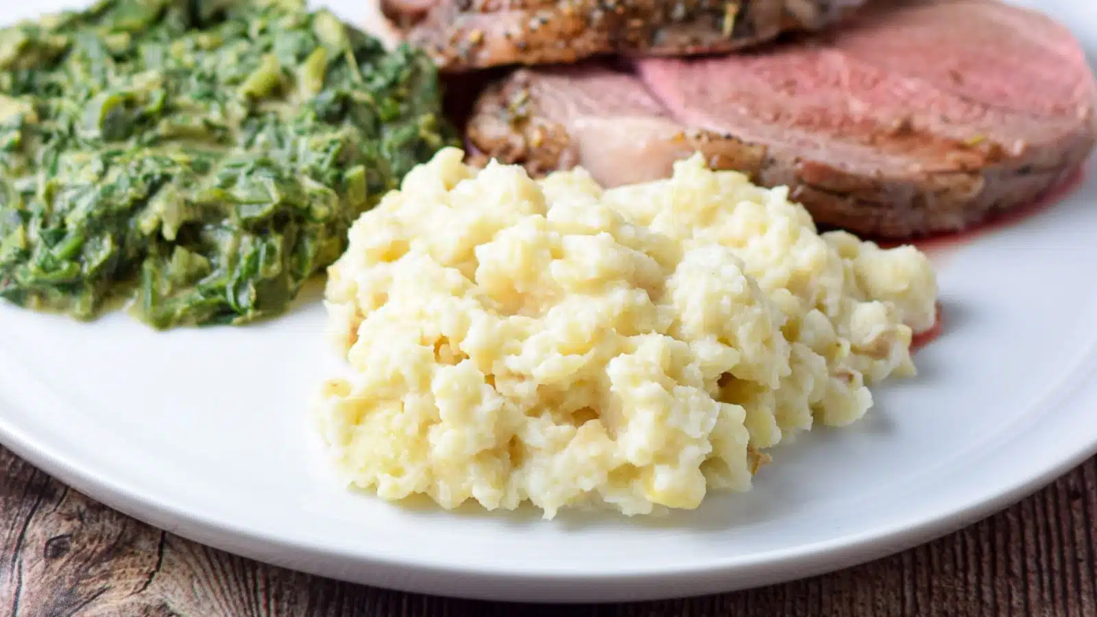 A white plate with mashed celery root, spinach, and lamb
