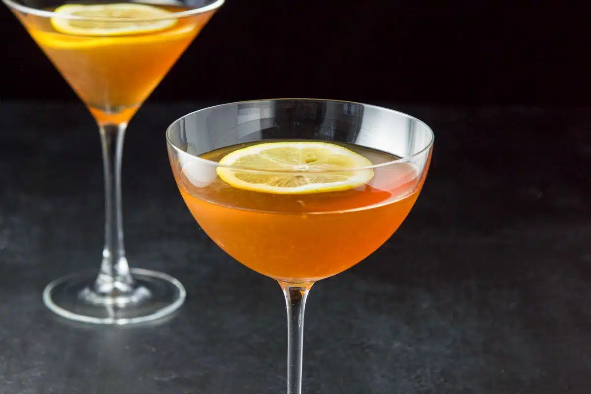 two martini glasses with the amber cocktail in it with a lemon wheel floating in the liquid