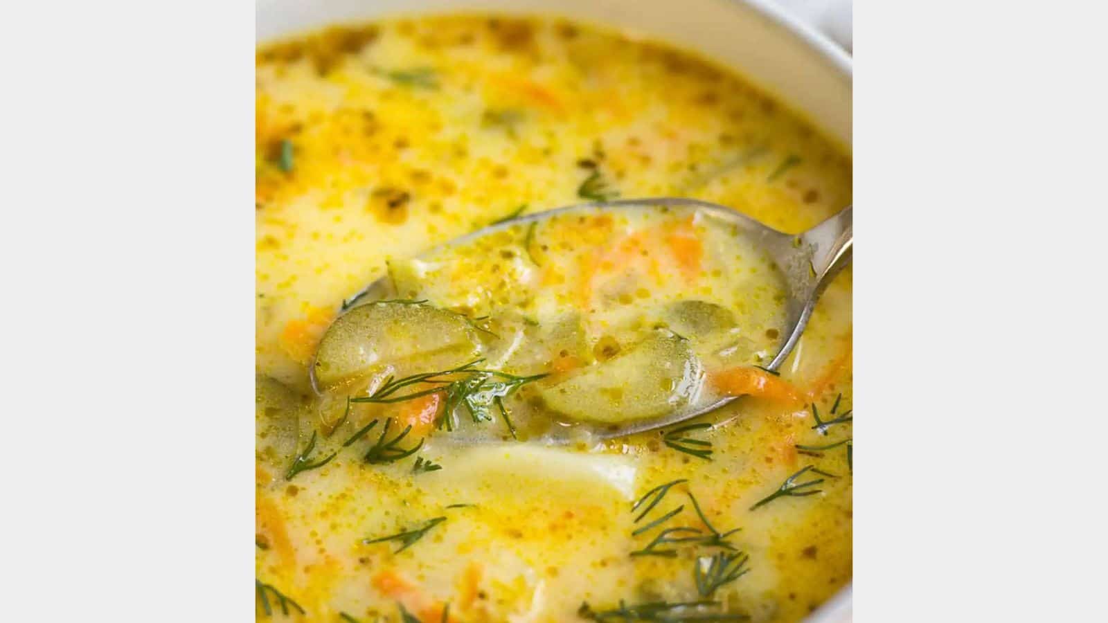 A spoon in a pickle soup with dill on top