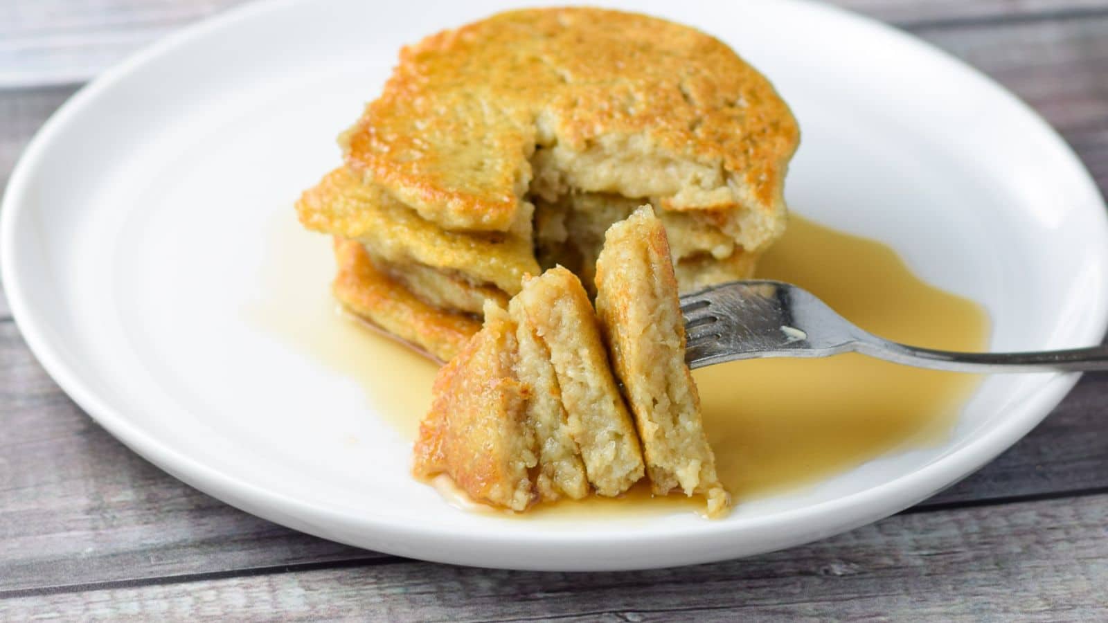 horizontal photo of a white plate of pancakes with some cut triangles on a fork