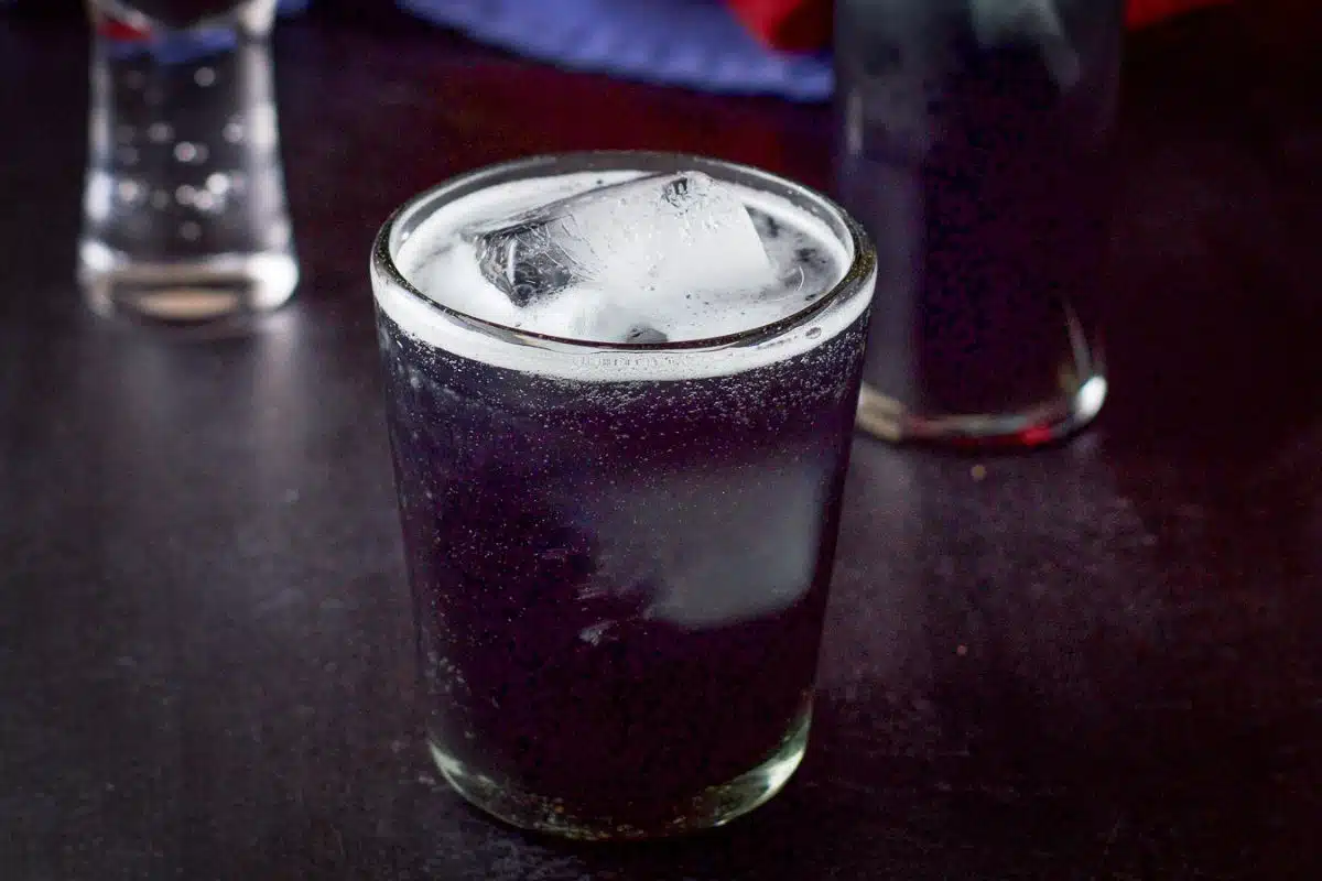 a glass filled with the purple cocktail with two other glasses in the back