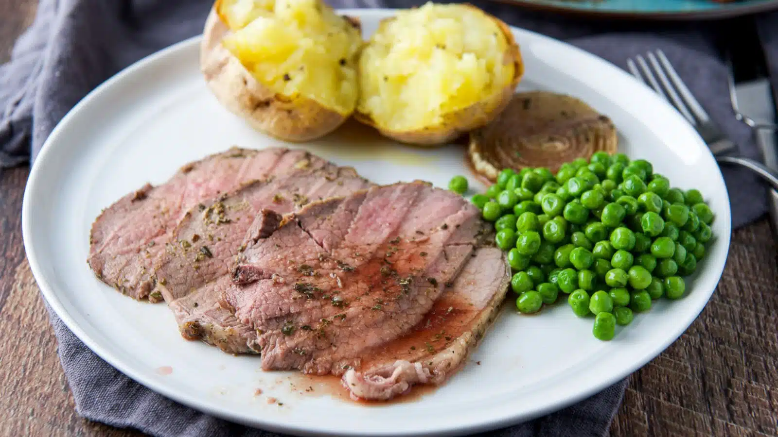 a horizontal photo of a white plate with vegetables and three slices of roast beef with juice on it