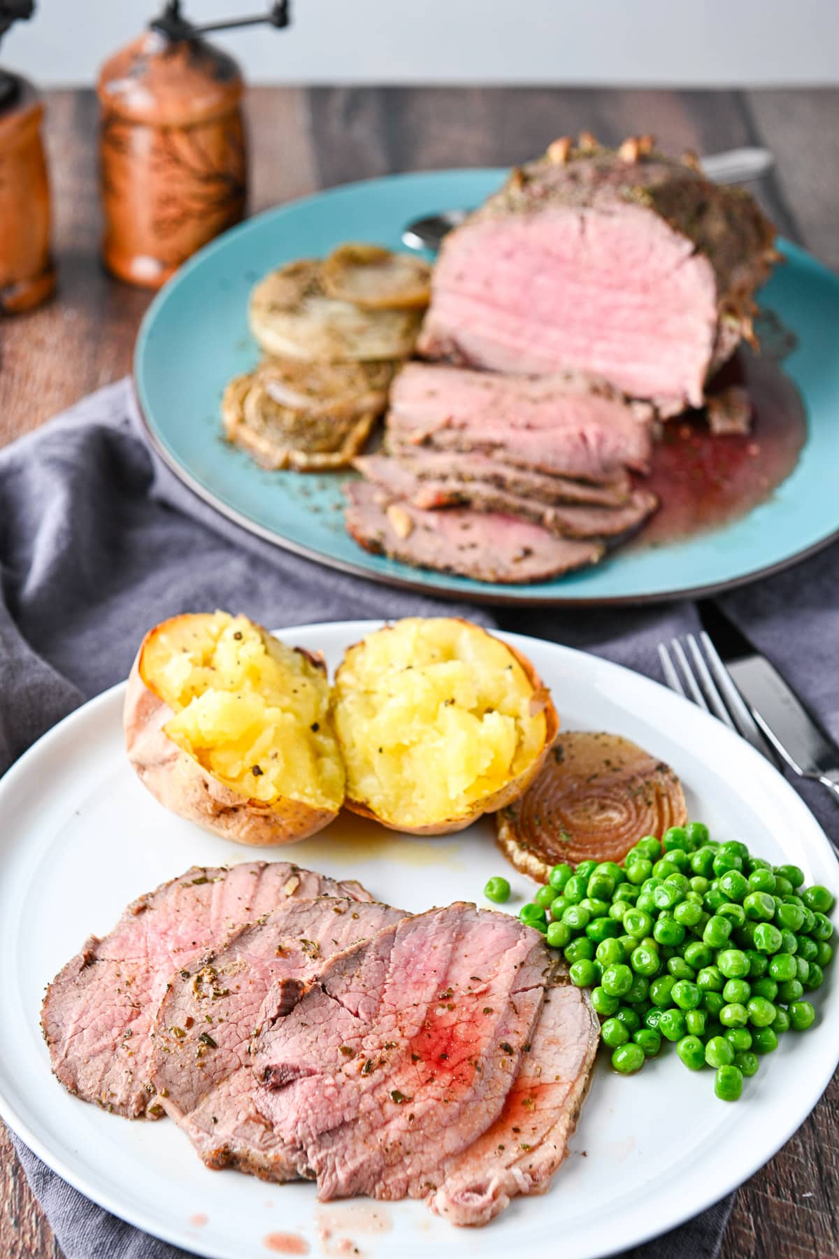 A table with a platter of meat along with a white plate with slices of beef and vegetables
