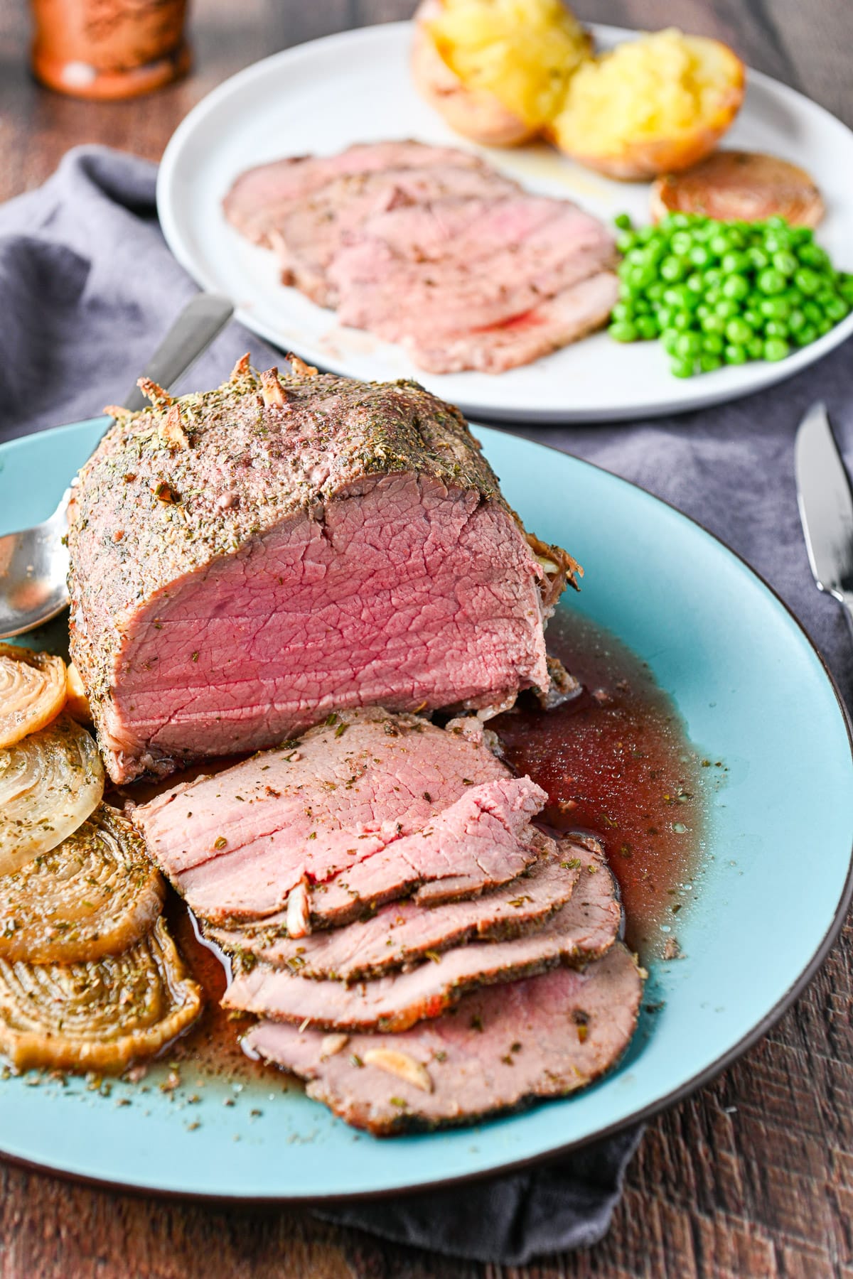 A blue platter with a beef roast on it that has been sliced - there is also a plate of the meal behind it