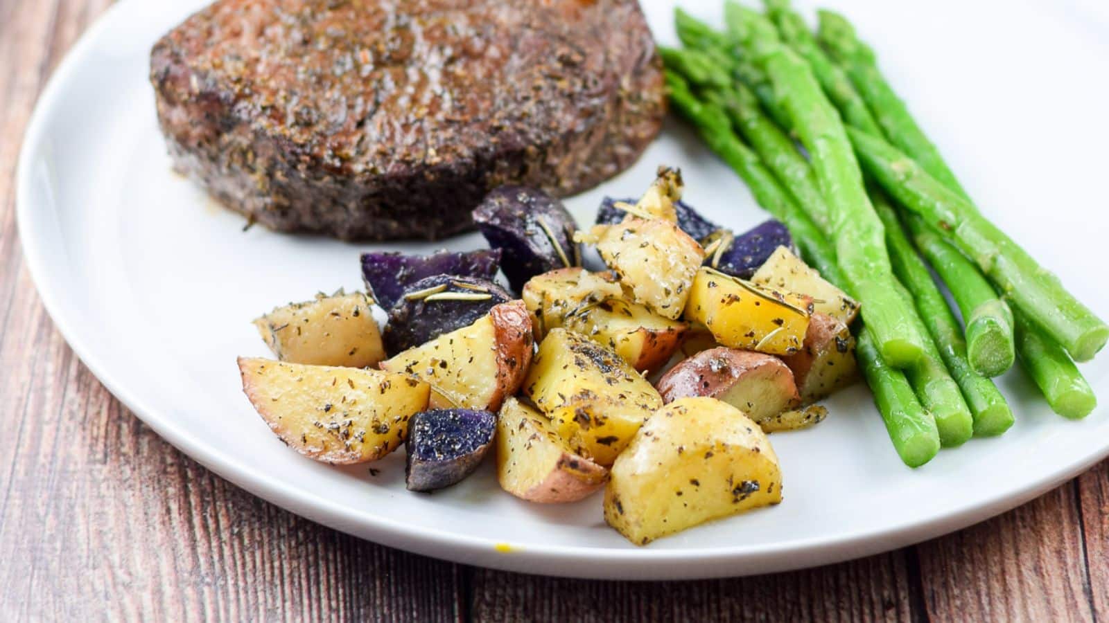 a white plate with potatoes, asparagus, and steak