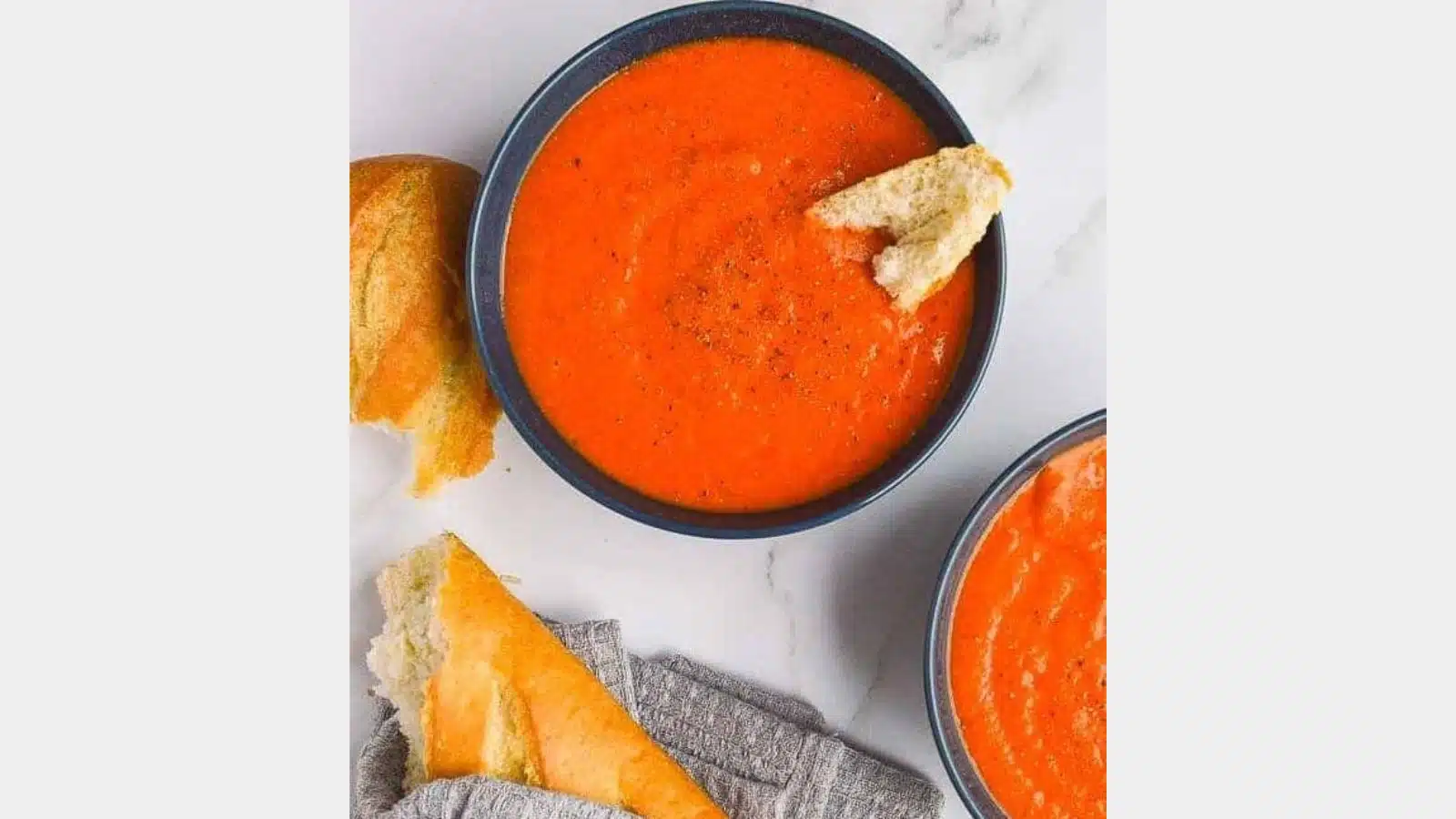 two dark bowls filled with red soup and bread on the side and in the soup