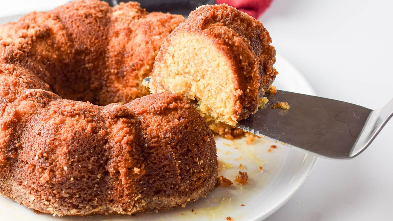 A cake cutter holding a piece of bundt cake above the cake