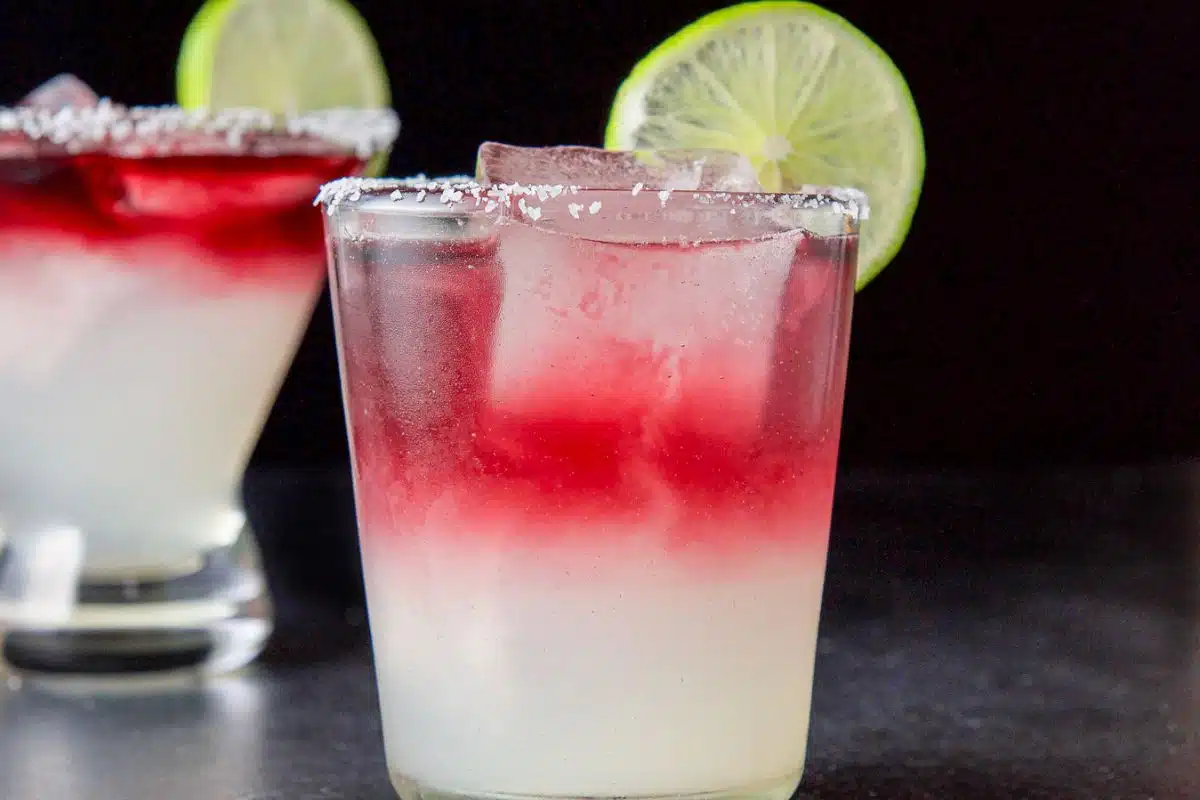 two glasses in vertical view with the two-toned margarita in it - red on top of lime