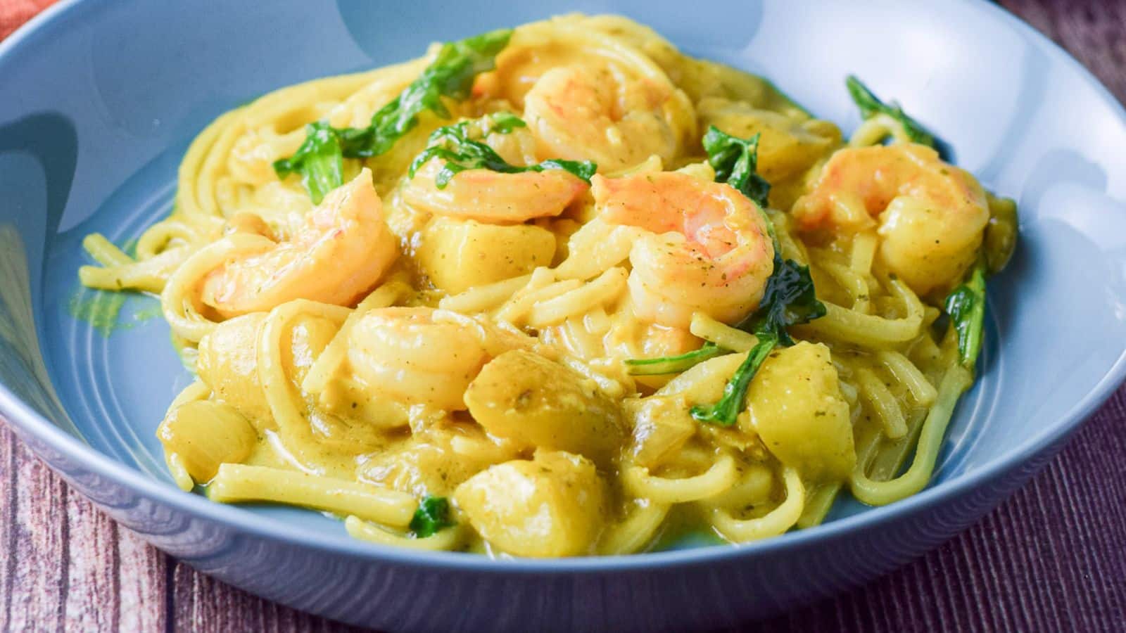 A blue deep bowl filled with noodles, shrimp and vegetables