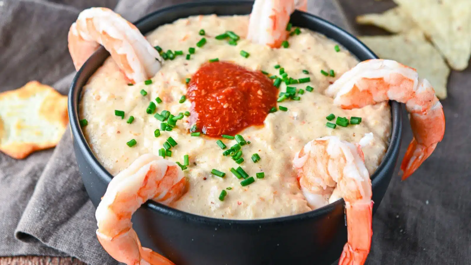 A black bowl filled with a dip with shrimp on the side and cocktail sauce in the middle