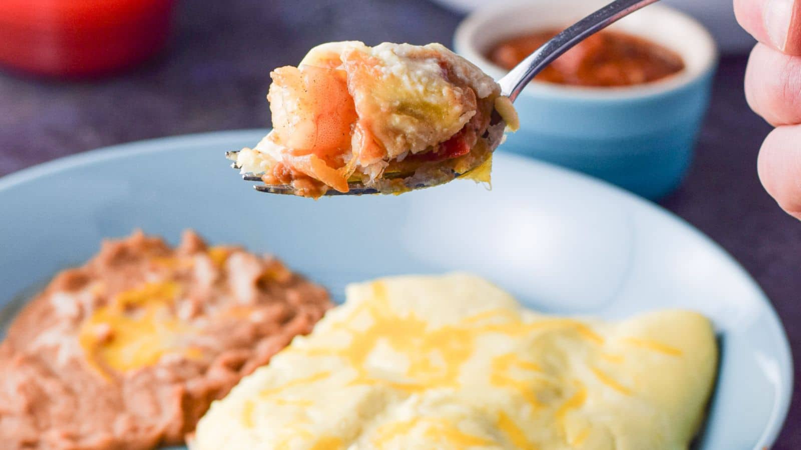 a hand holding a fork filled with the shrimp held over the plate of enchiladas and beans