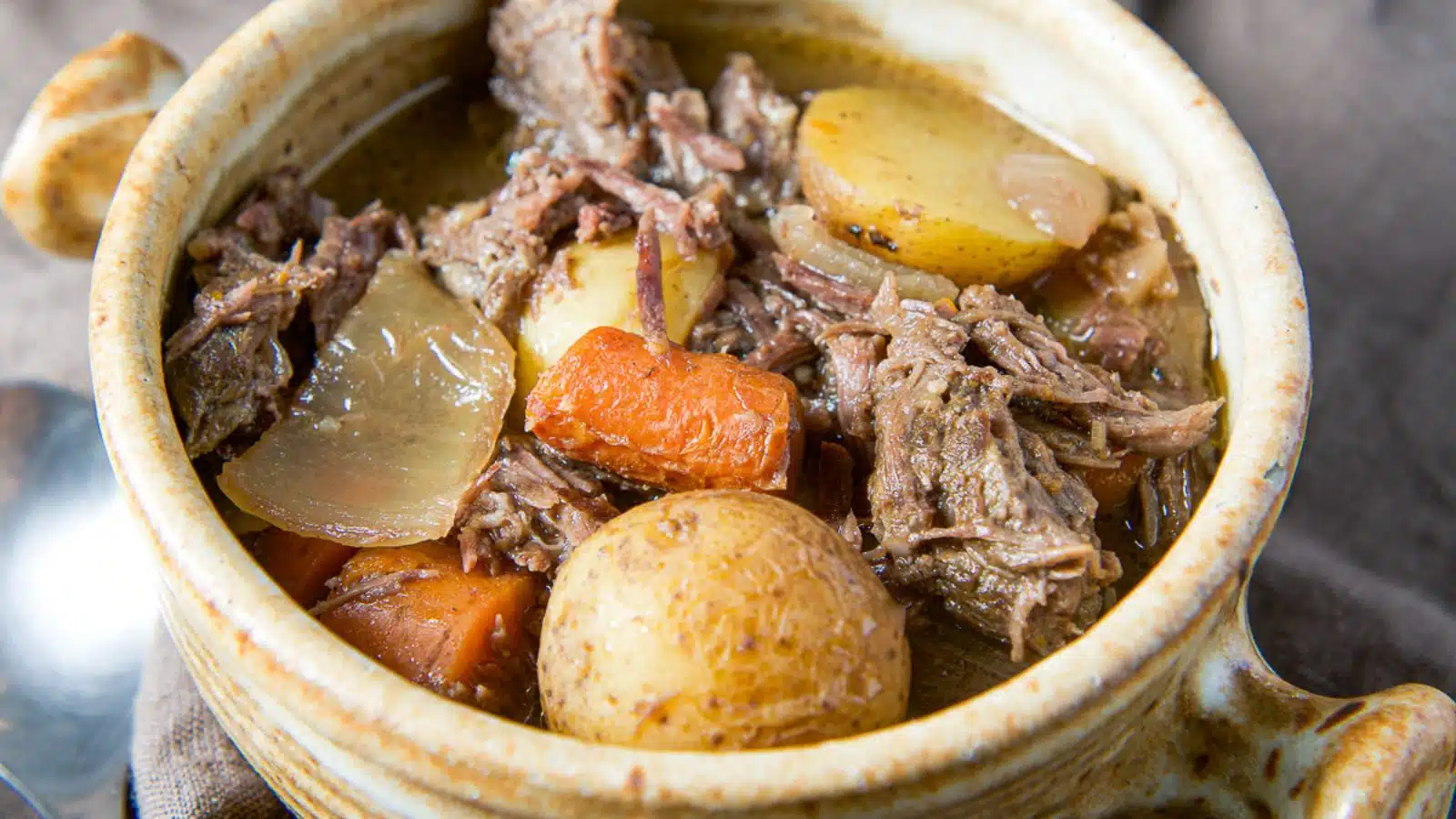 a crock with potatoes, shredded beef, onions and carrots with a gravy