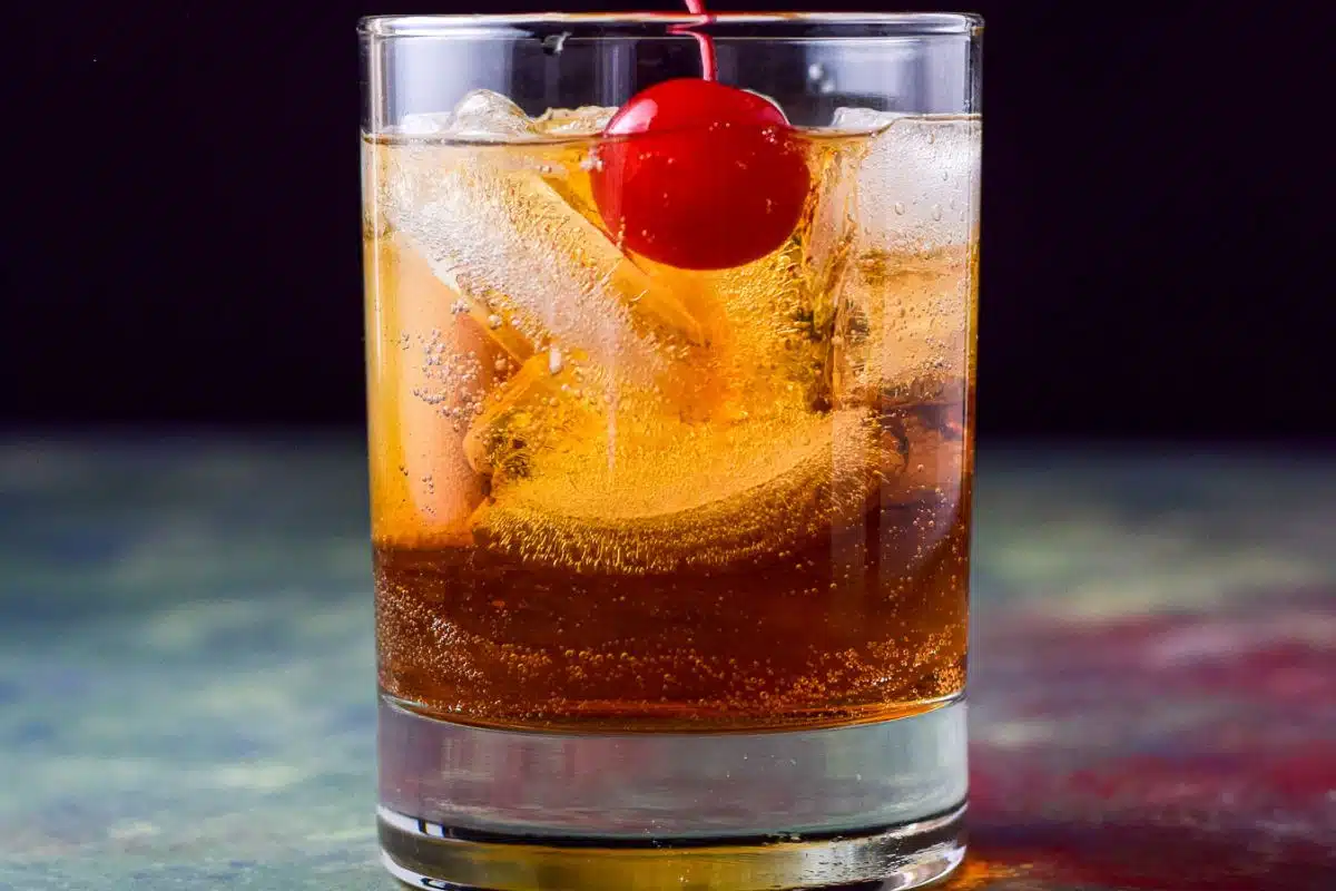 A short glass with the manhattan in it with a red cherry