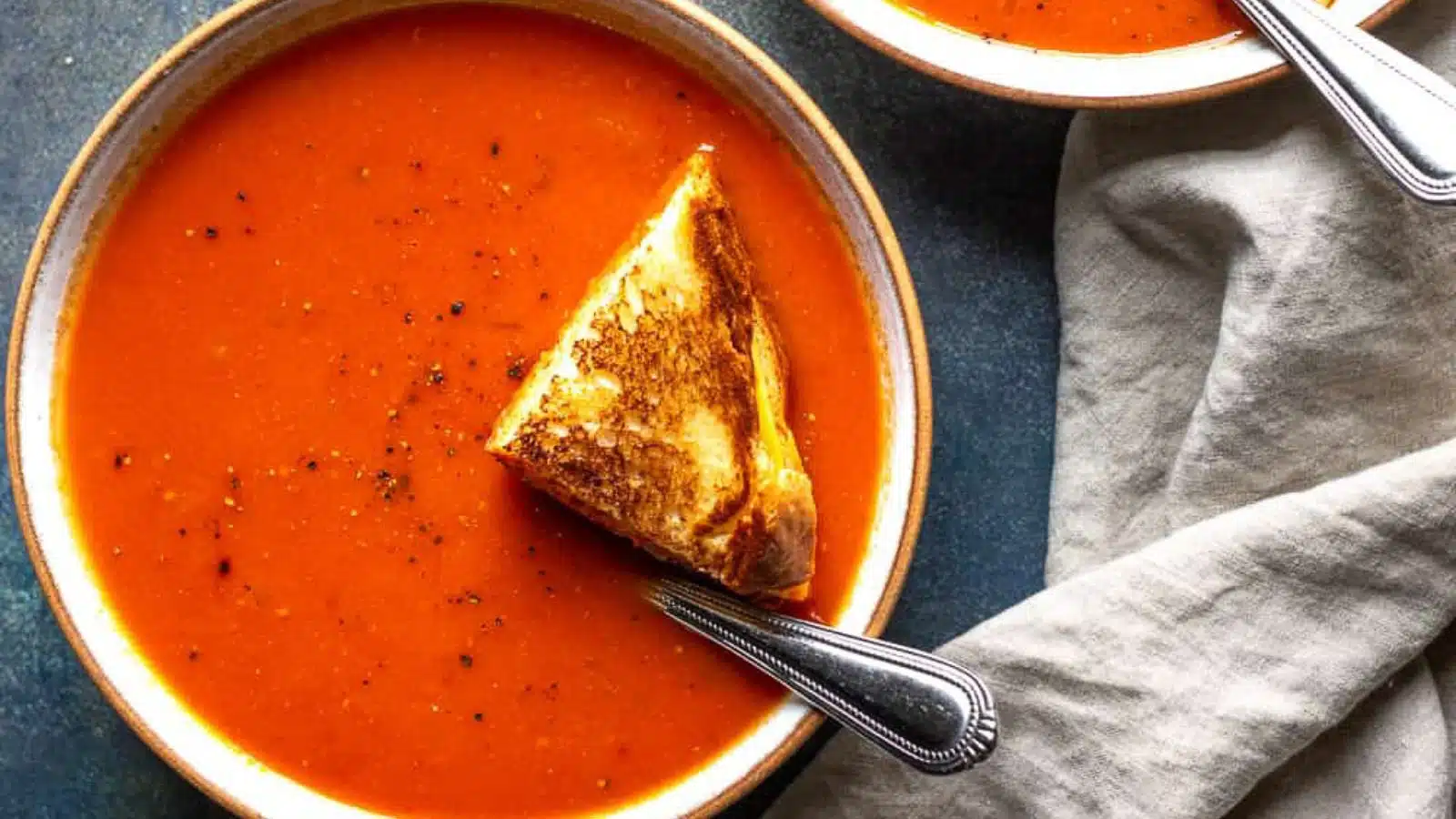 overhead view of a bowl of tomato soup with cracked pepper and a grilled sandwich wedge