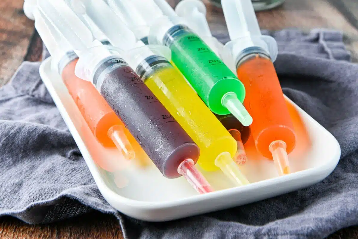 A white platter with large syringes filled with colorful jello
