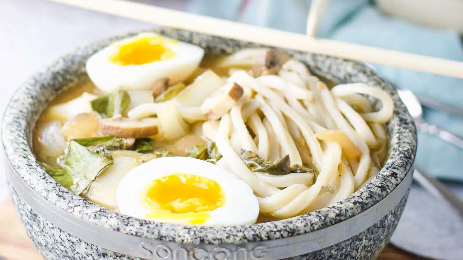 a stone bowl filled with udon noodles, egg halves and soup