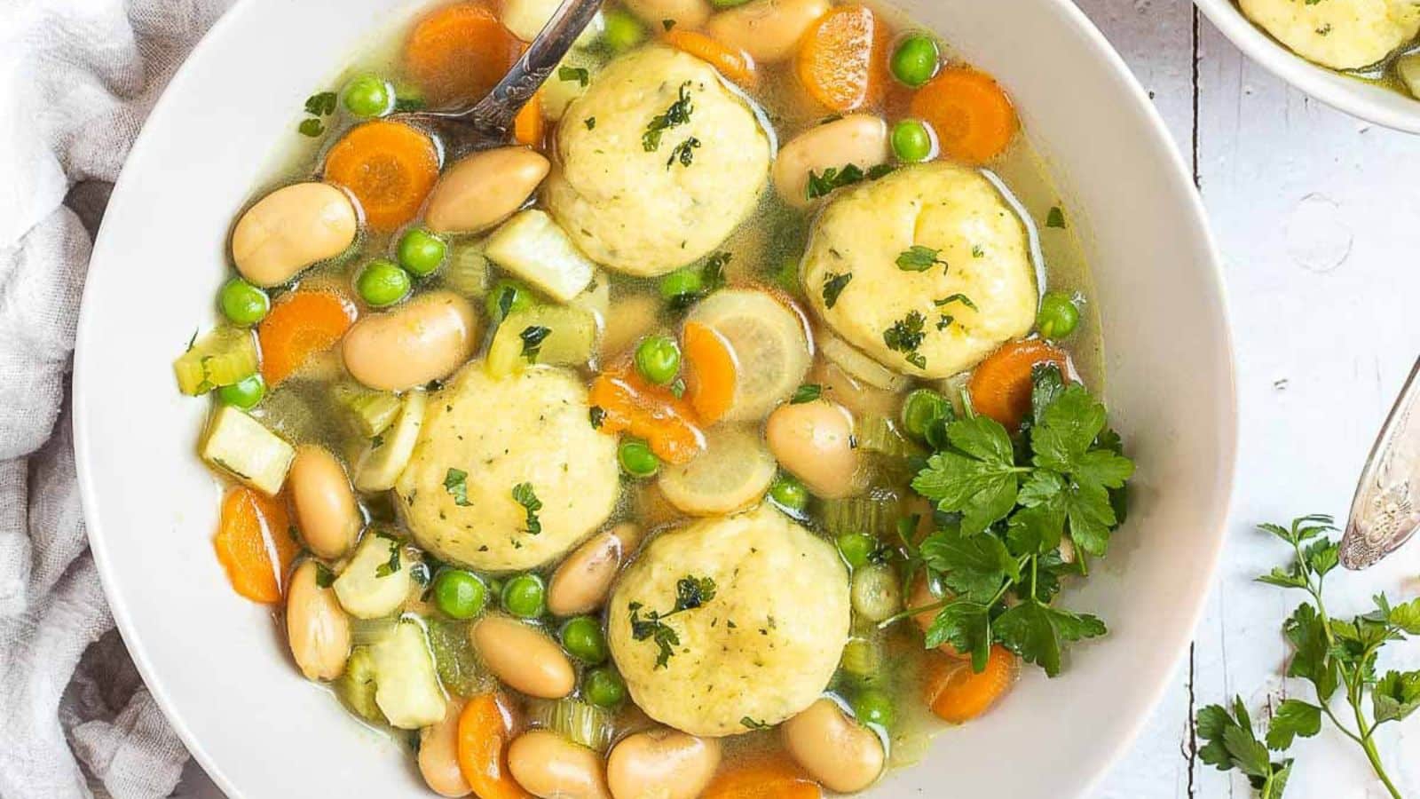 Overhead view of a white bowl with soup with dumplings, vegetables, and beans
