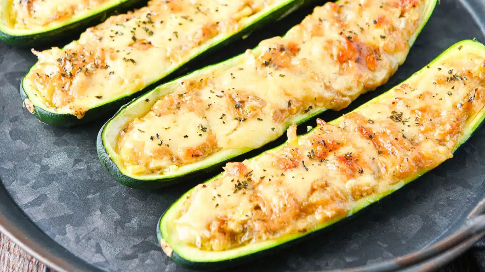 a metal dish with zucchini halves with melted cheese on top