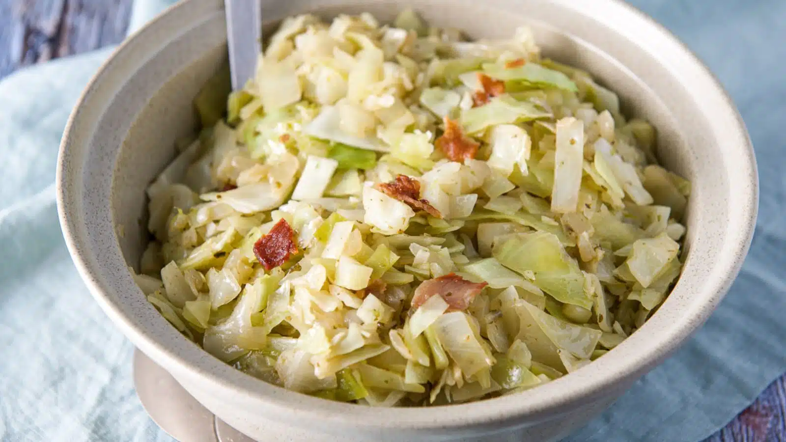 A bowl with cabbage and bacon on a blue napkin