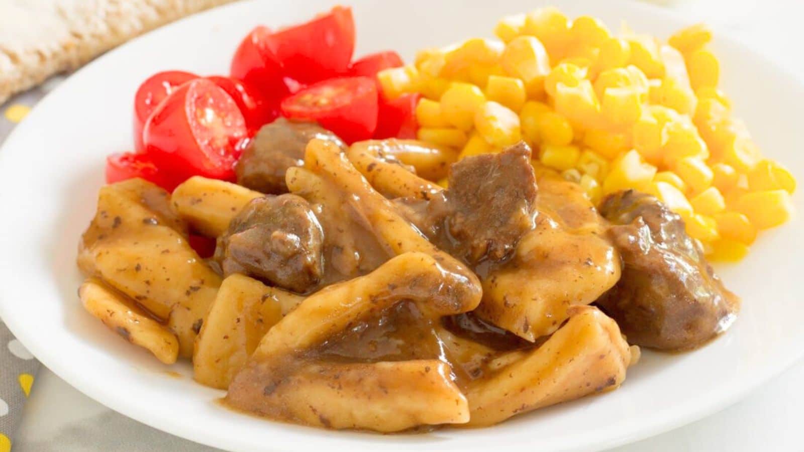 A white plate with noodles with beef and gravy along with tomatoes and carrots