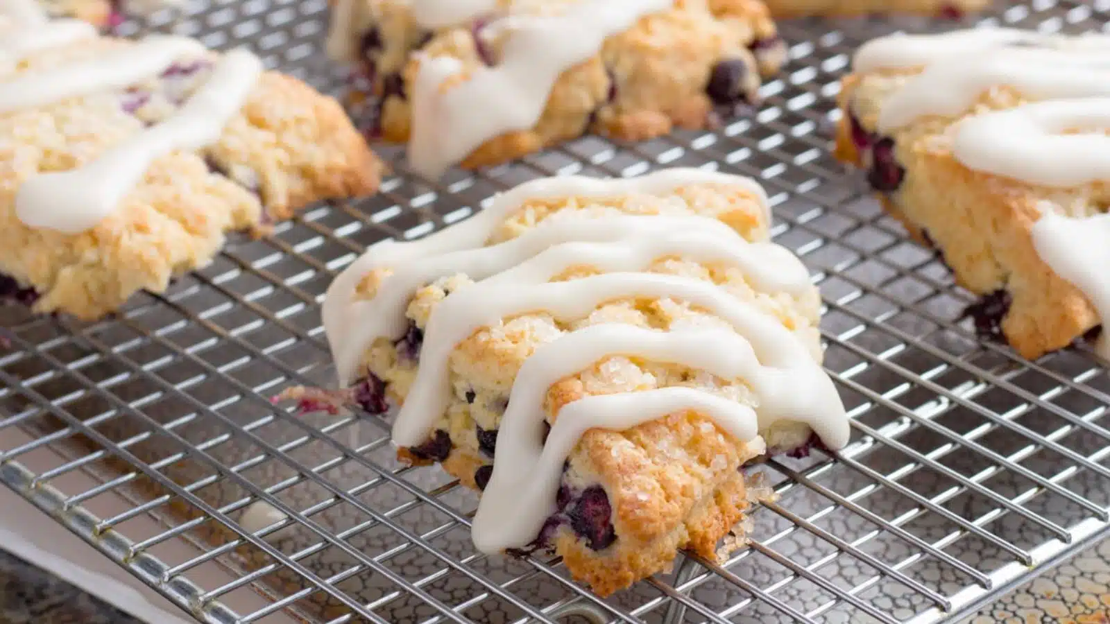 A wire rack with glazed blueberry scones on it