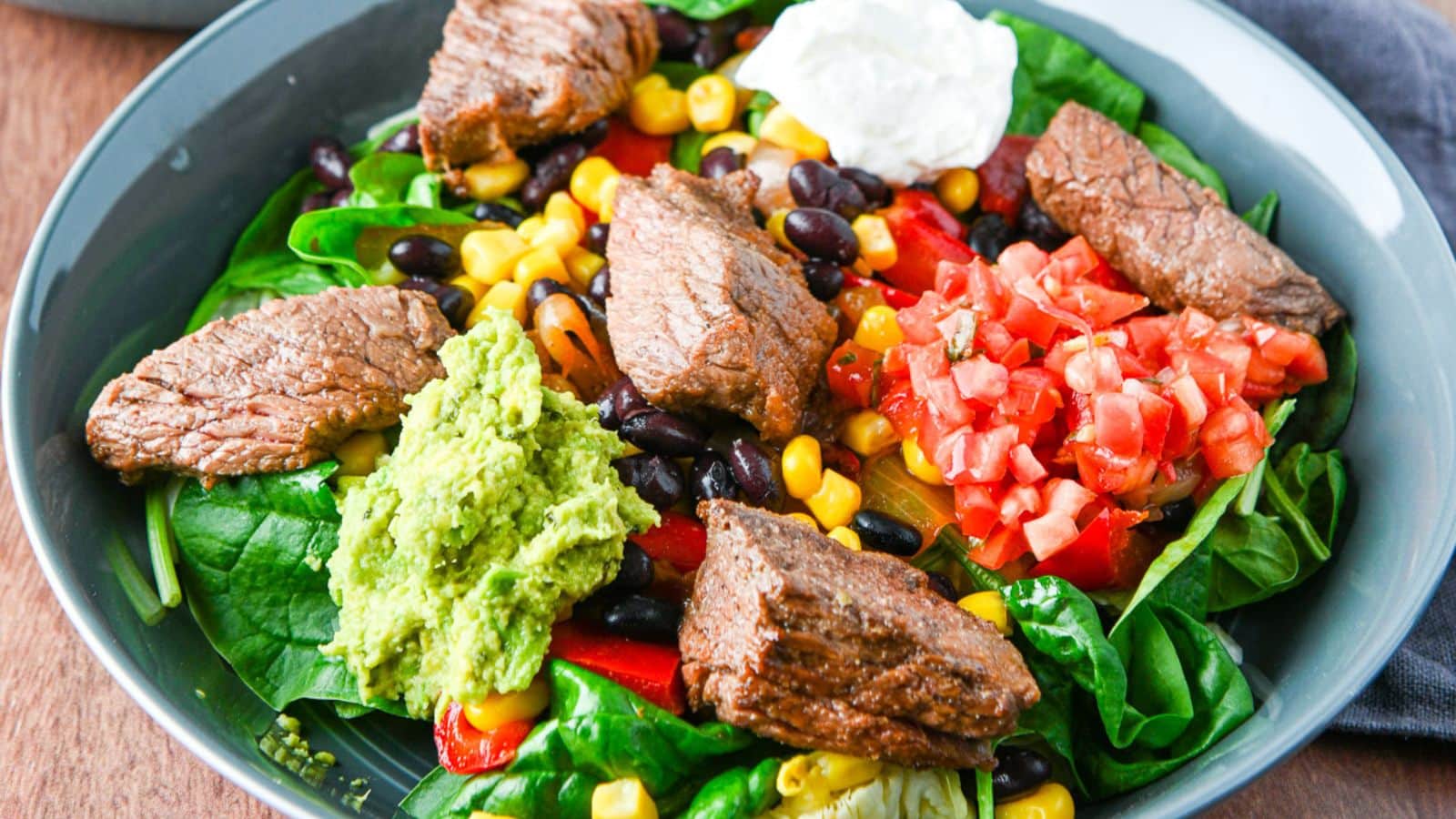 deep blue dish with veggies, corn, beans, salsa, beef, sour cream and guacamole