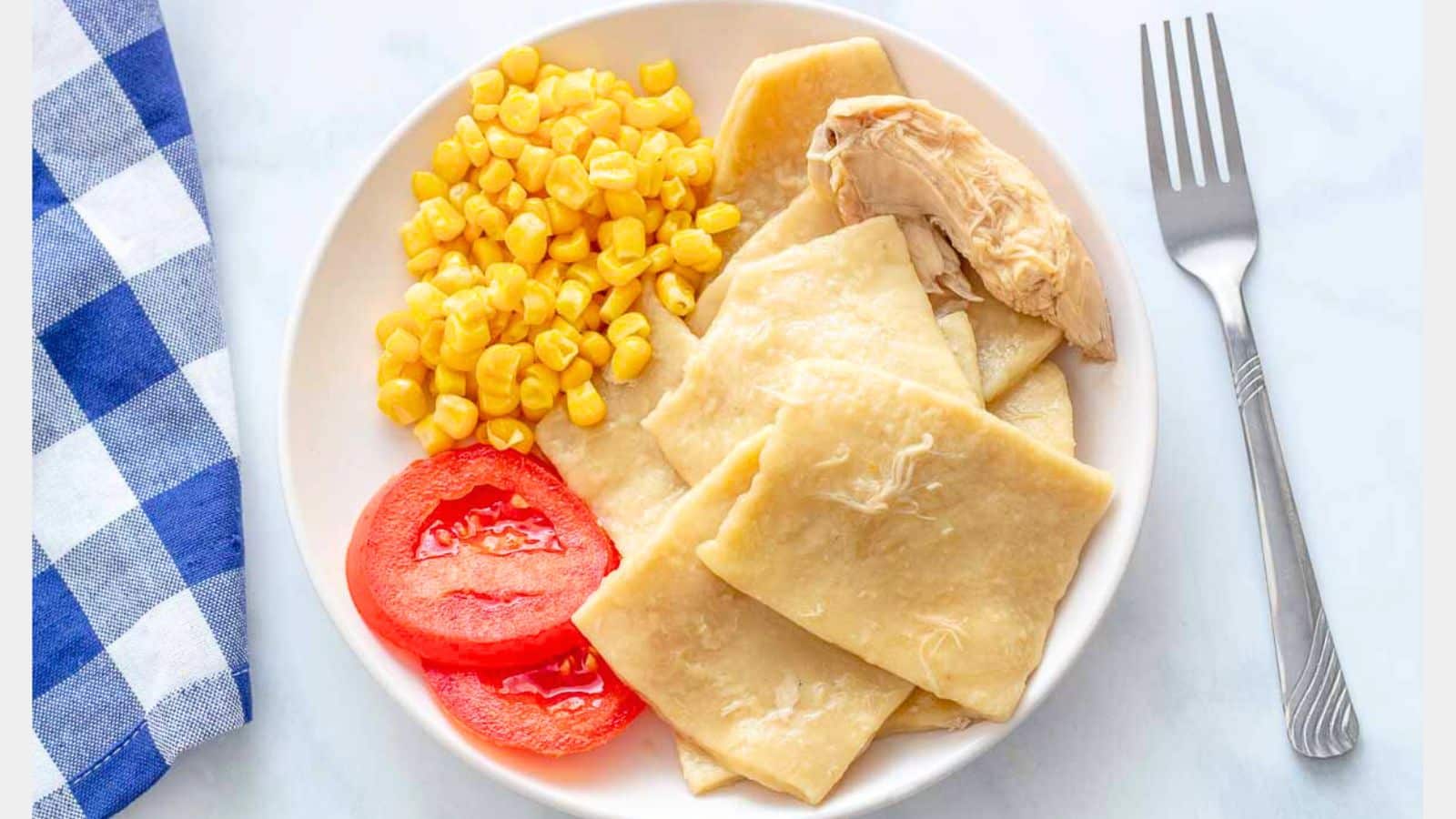 Overhead view of a white plate with chicken and dumplings with corn and tomato