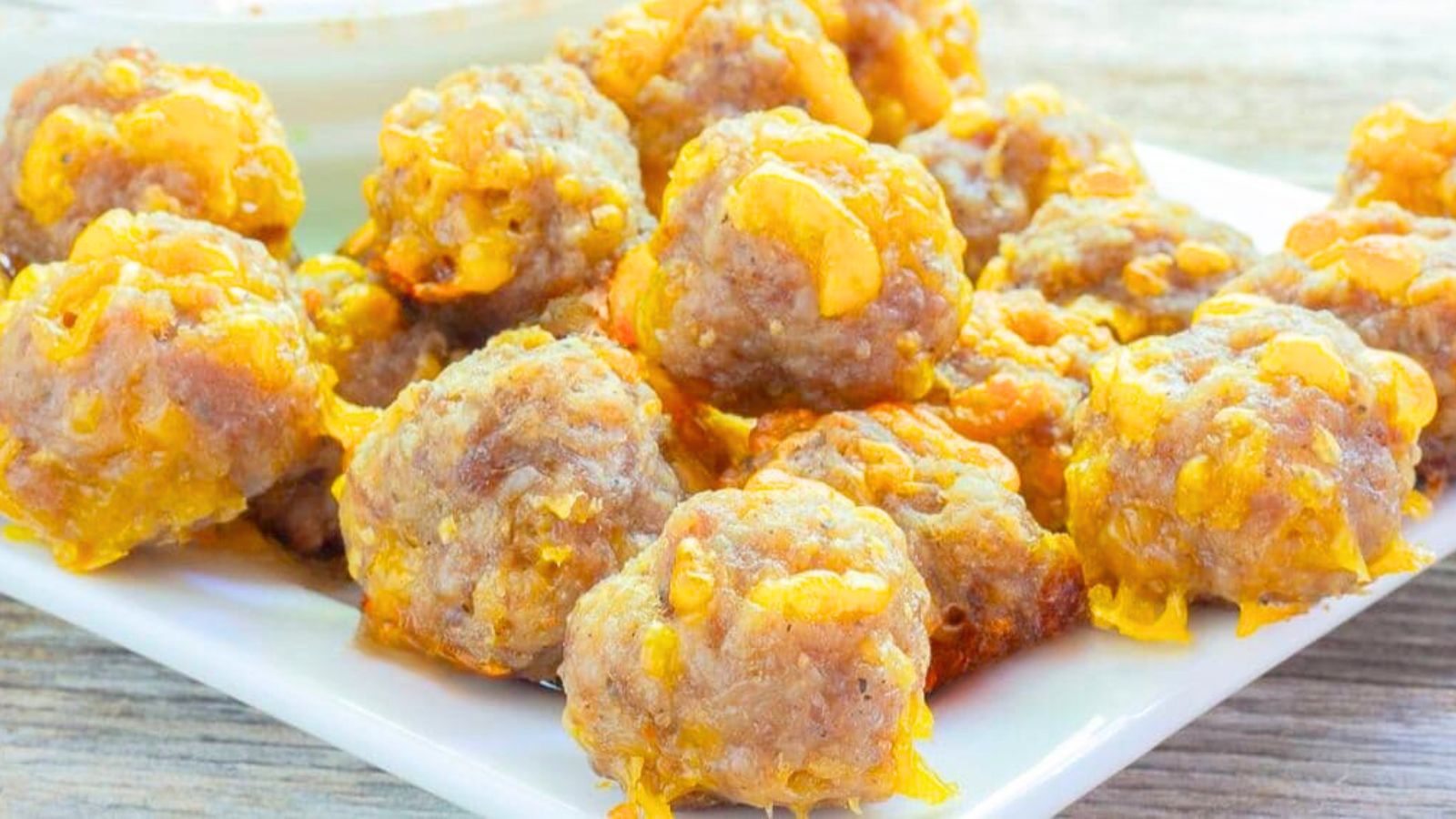 A square white plate with cheesy sausage meatballs on it