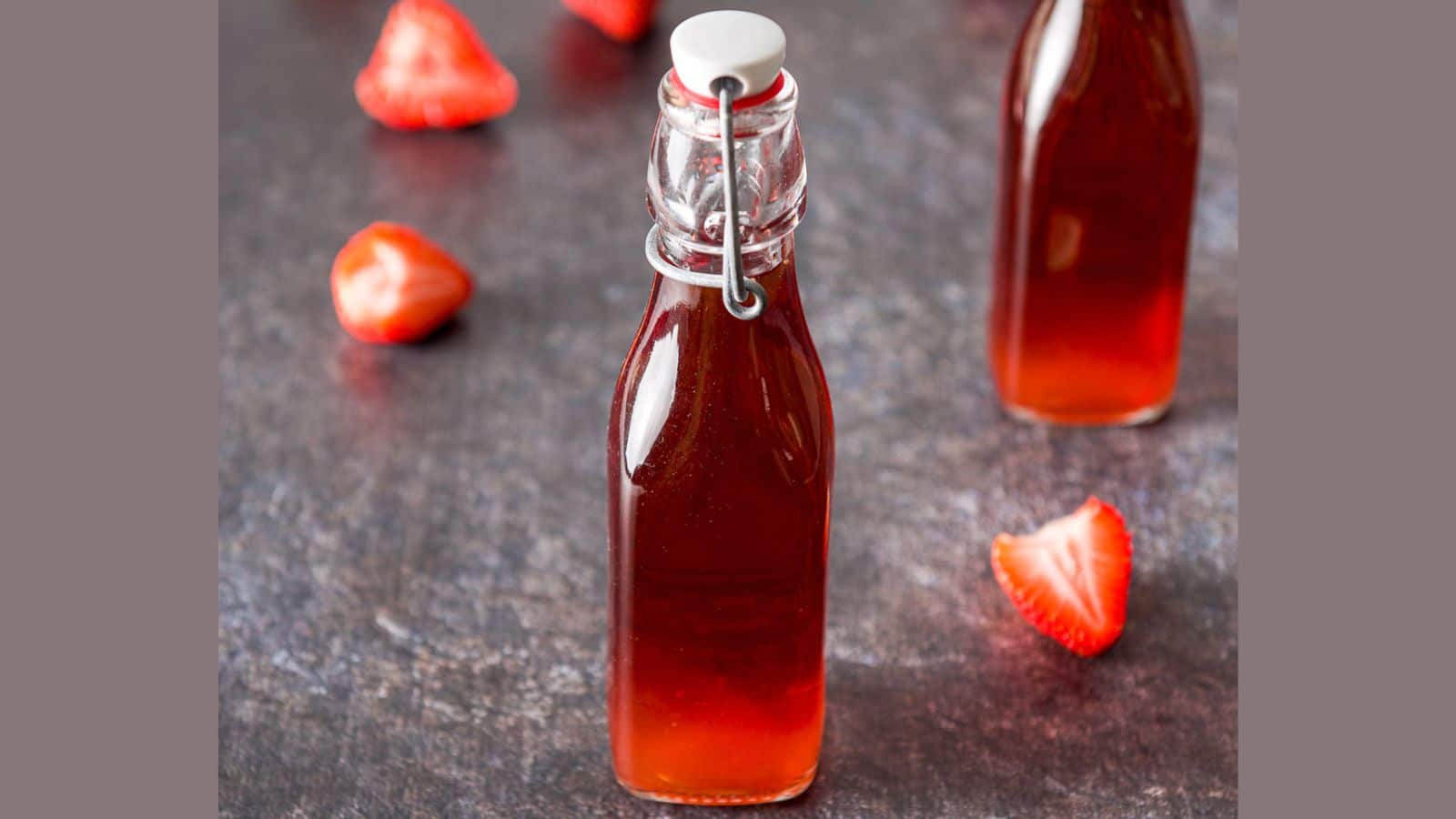 Two small glass bottles with strawberry vodka in them with more strawberries on the table