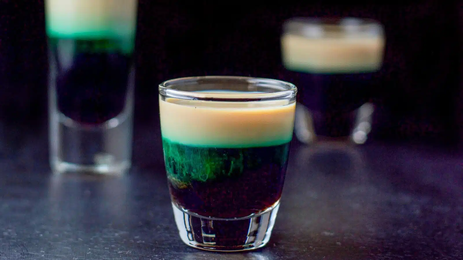 three shot glasses with a green, beige, and brown liquor layered in them