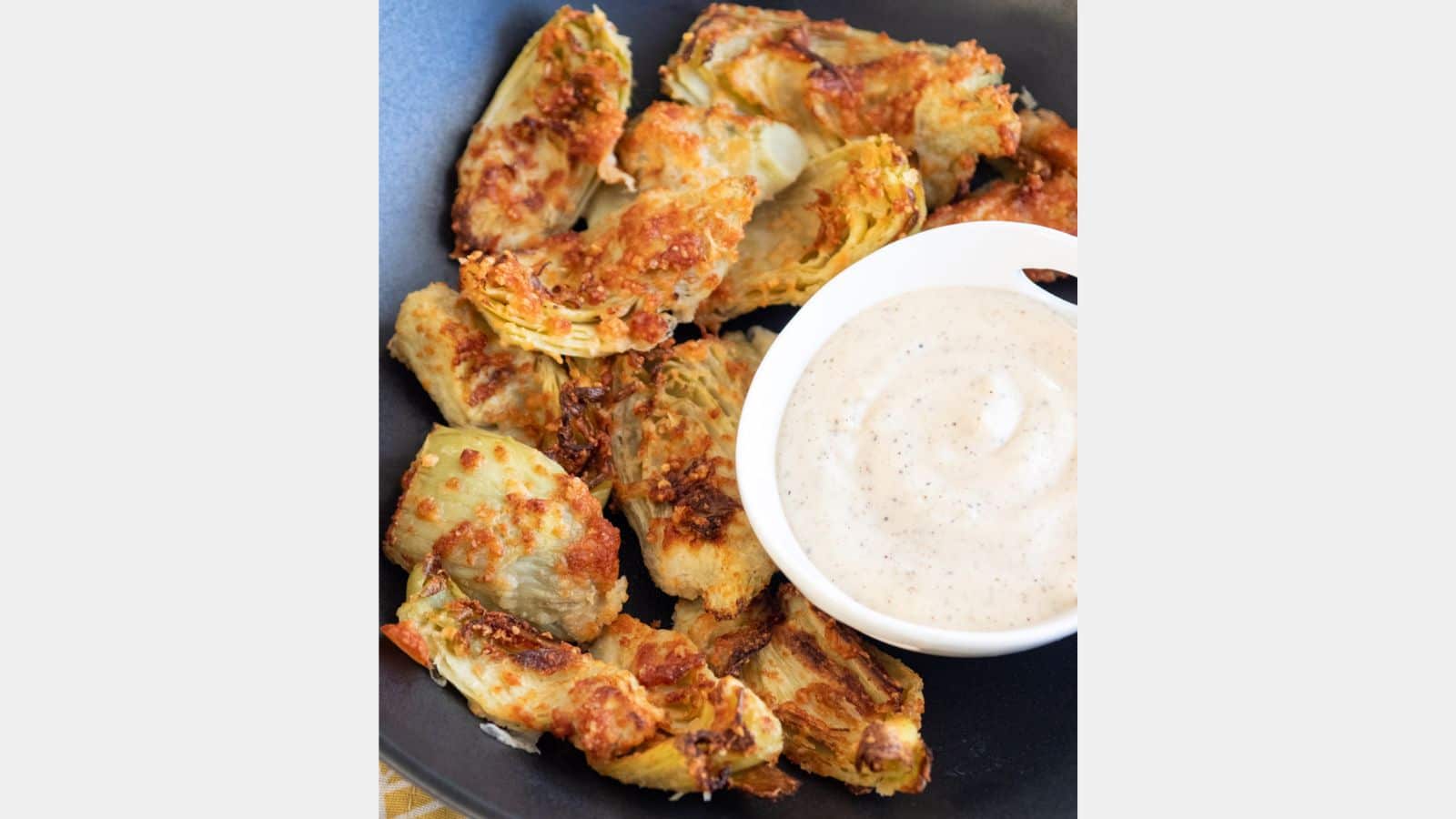 A bowl of aioli with fried artichokes in a black bowl