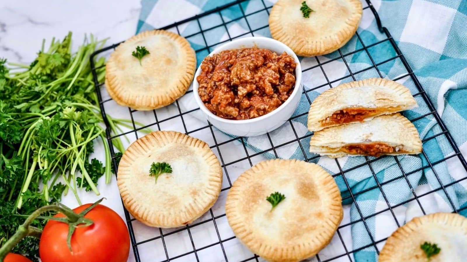 a wire rack with hand pies on it and a bowl of sloppy joes along with tomatoe and parsley