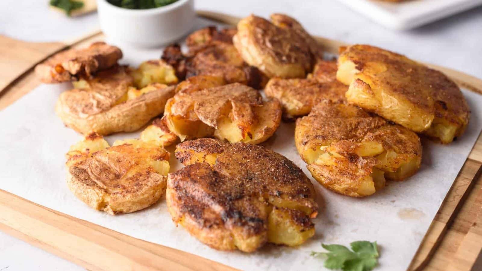 A board with smashed potatoes on it with some fresh parsley