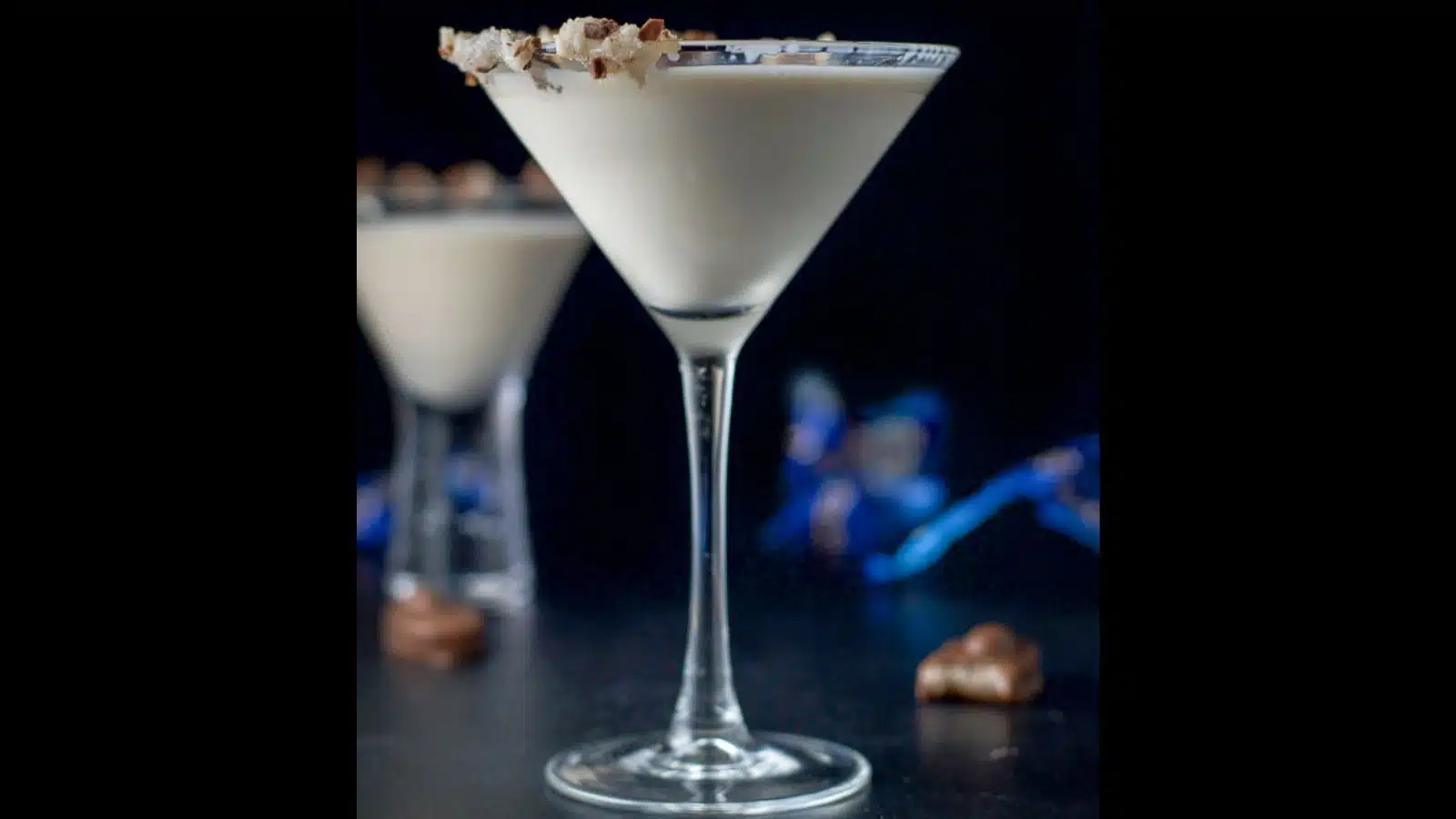 Two martini glasses filled with the cream drink with almond joy candy's on the table and on the rim