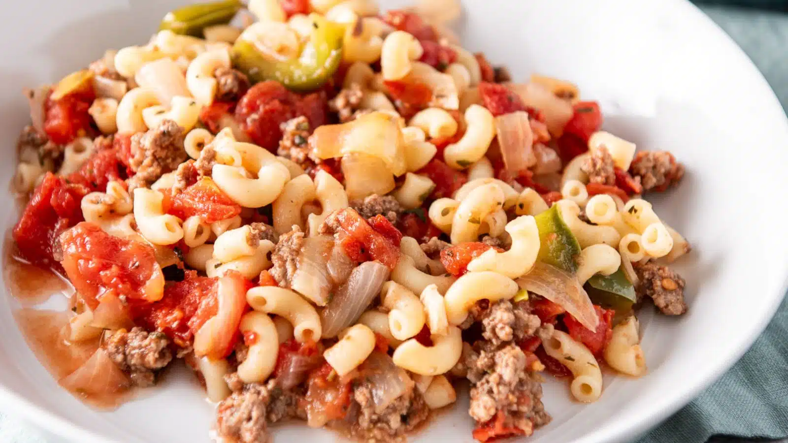 A white deep dish with elbow macaroni, tomatoes, ground beef, and green pepper