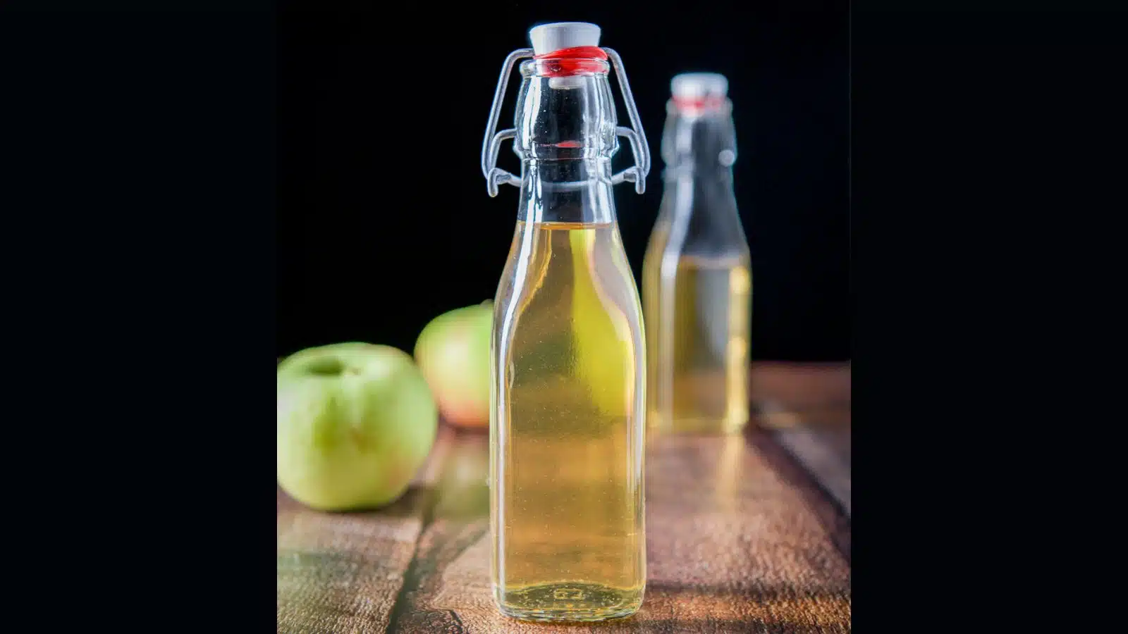 two glass bottles filled with apple vodka with two apples in the back