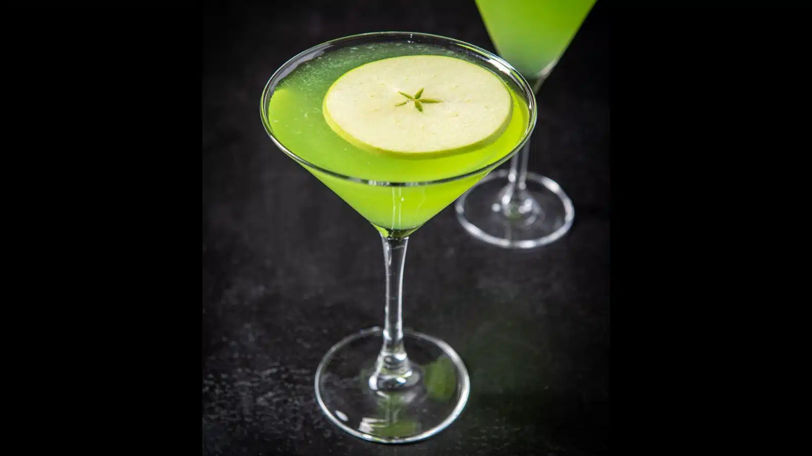 a martini glass filled with the green apple drink with an apple slice floating on the top