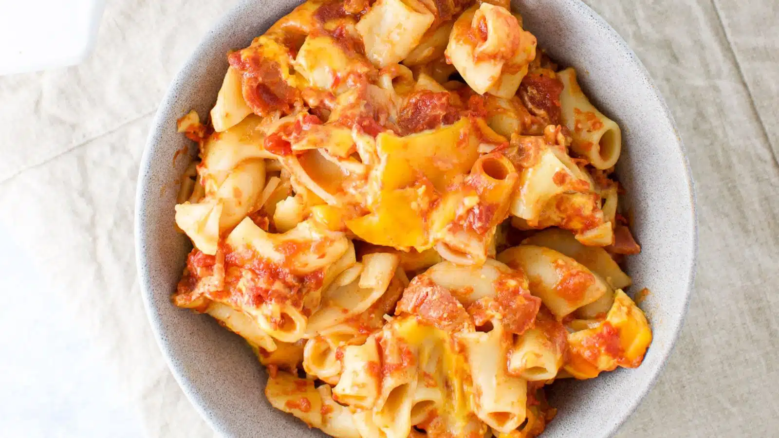 overhead view of elbow pasta with cheese, tomatoes and bacon in a grey bowl