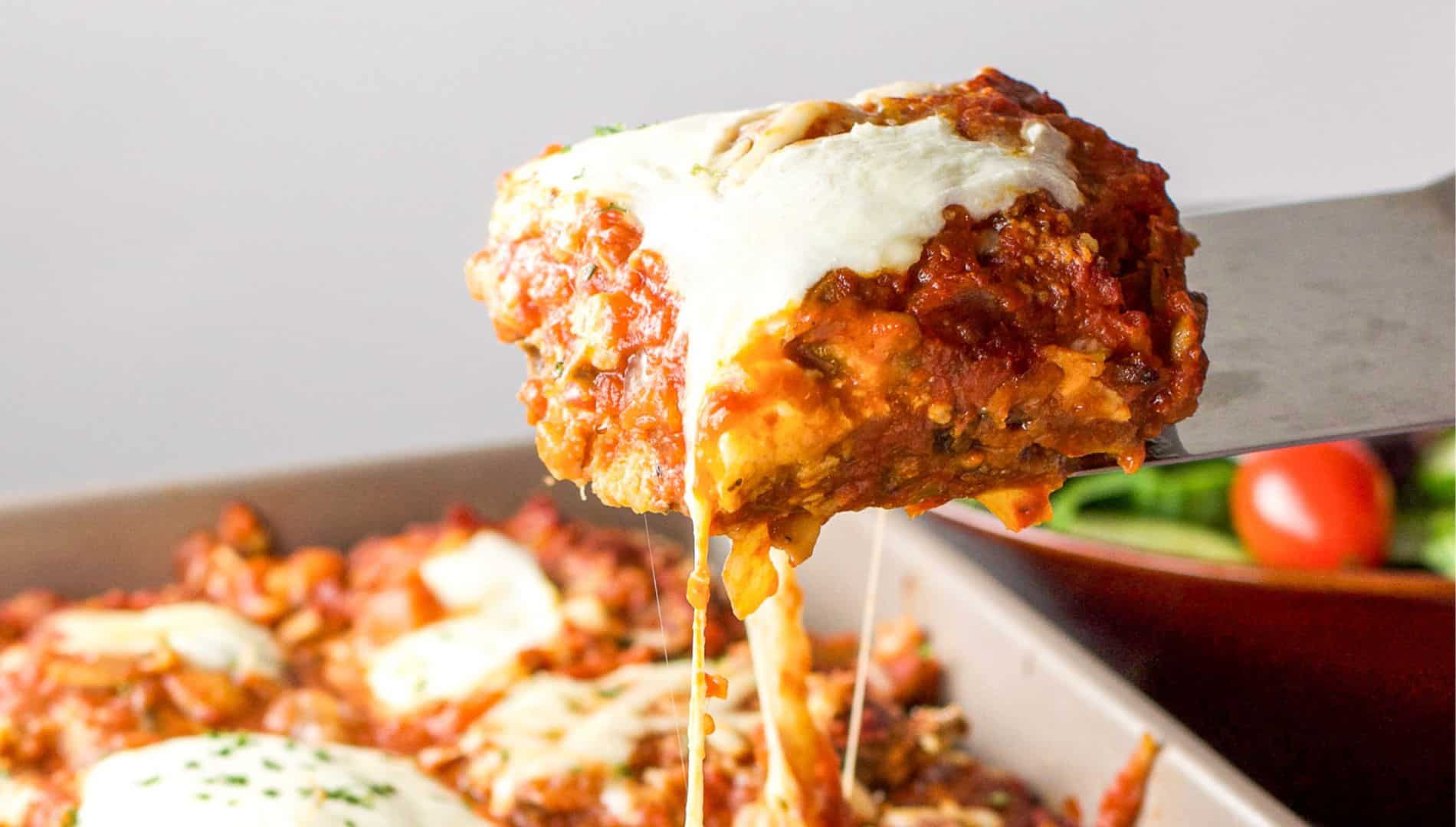a spatula holding up a square of eggplant parmesan over the pan