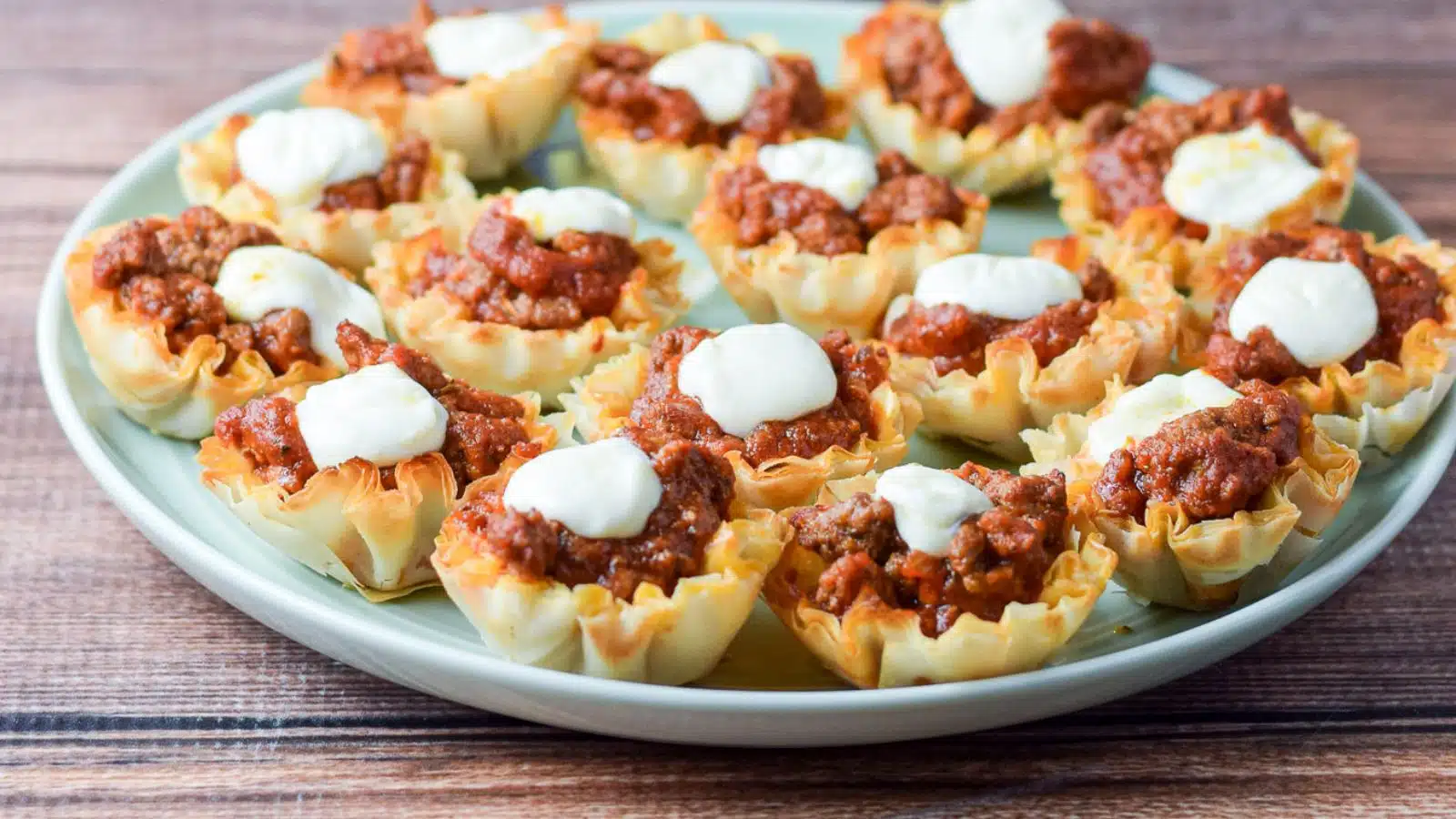 a green plate with phyllo cups filled with saucy beef and a pearl mozzarella ball