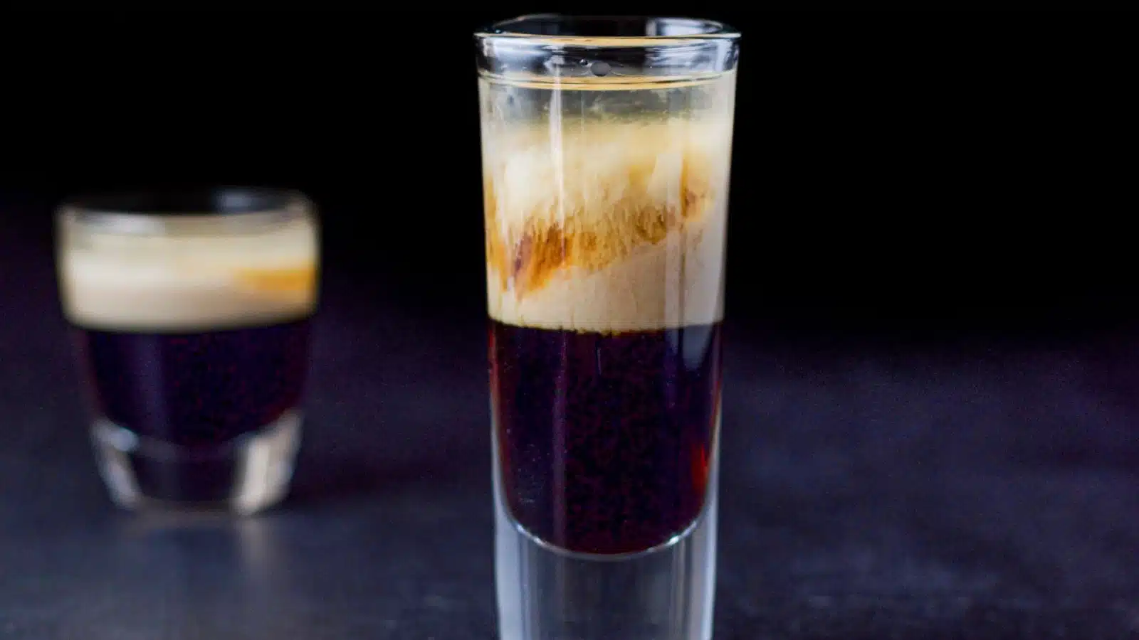 Two glasses, one tall and one short filled with the layered liqueur