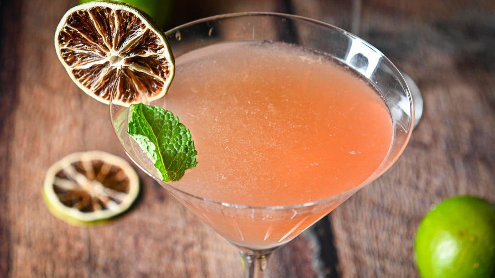 A martini glass with the juice cocktail with a mint leaf and dried lime wheels as garnish