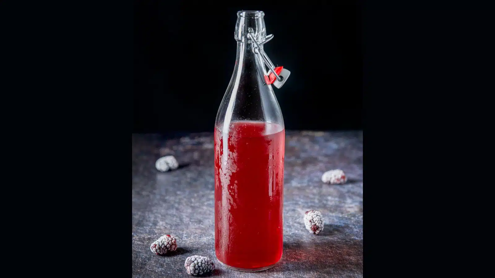 Frozen blackberries on a table with a bottle of blackberry vodka