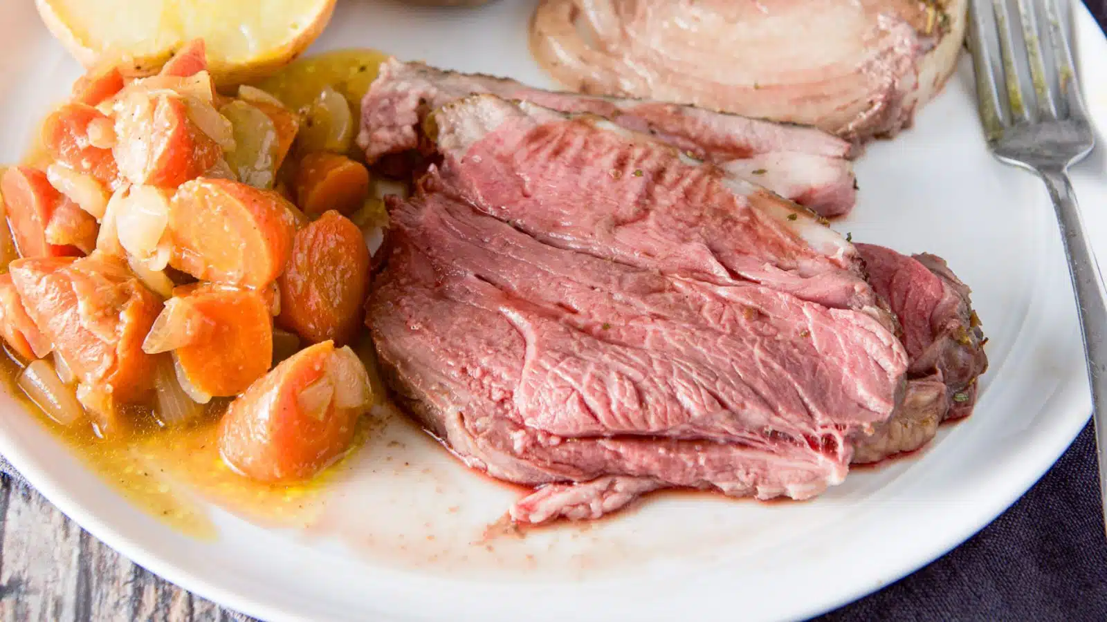 A white plate with a few pieces of lamb on it along with potato, carrots, and onion