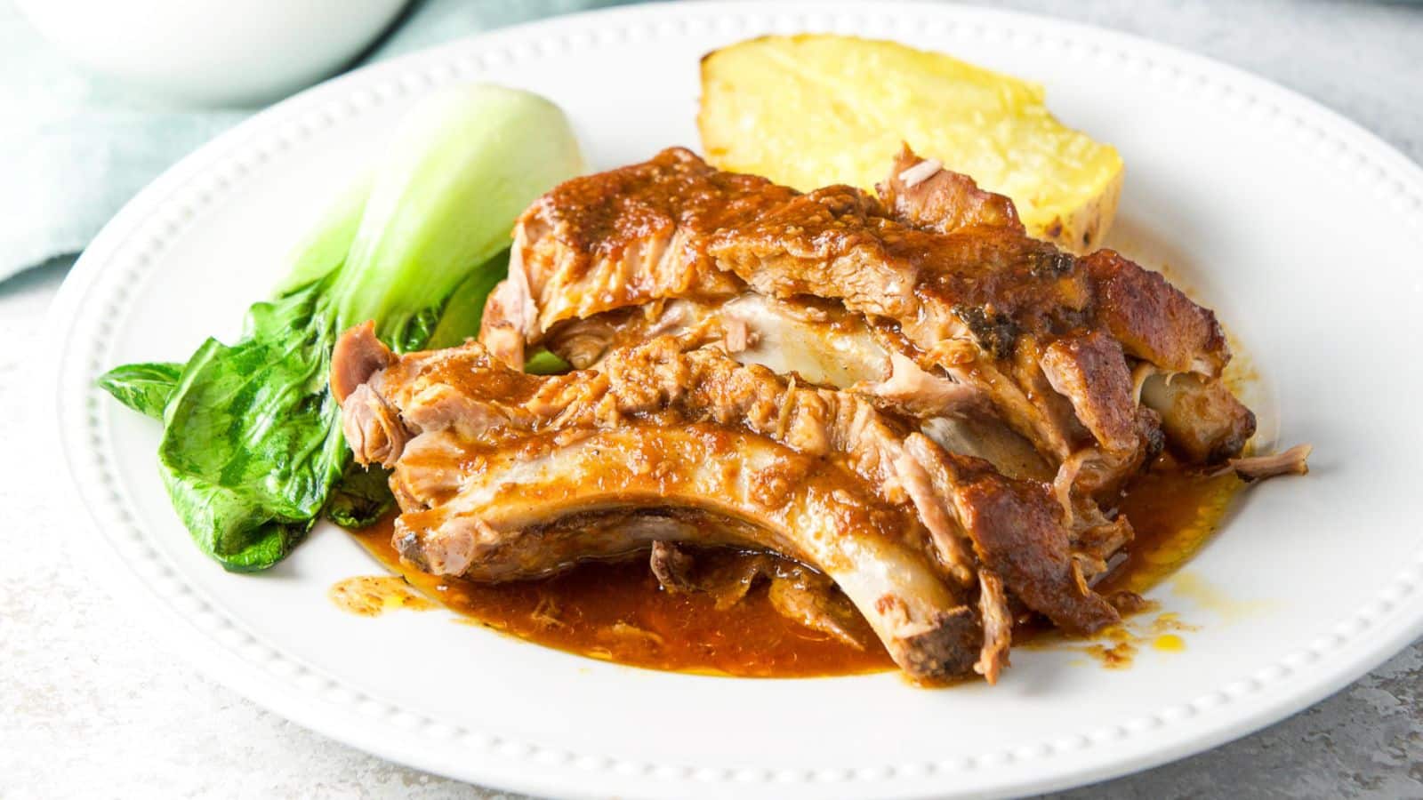 a white beaded plate with ribs on it with bok chow and potato