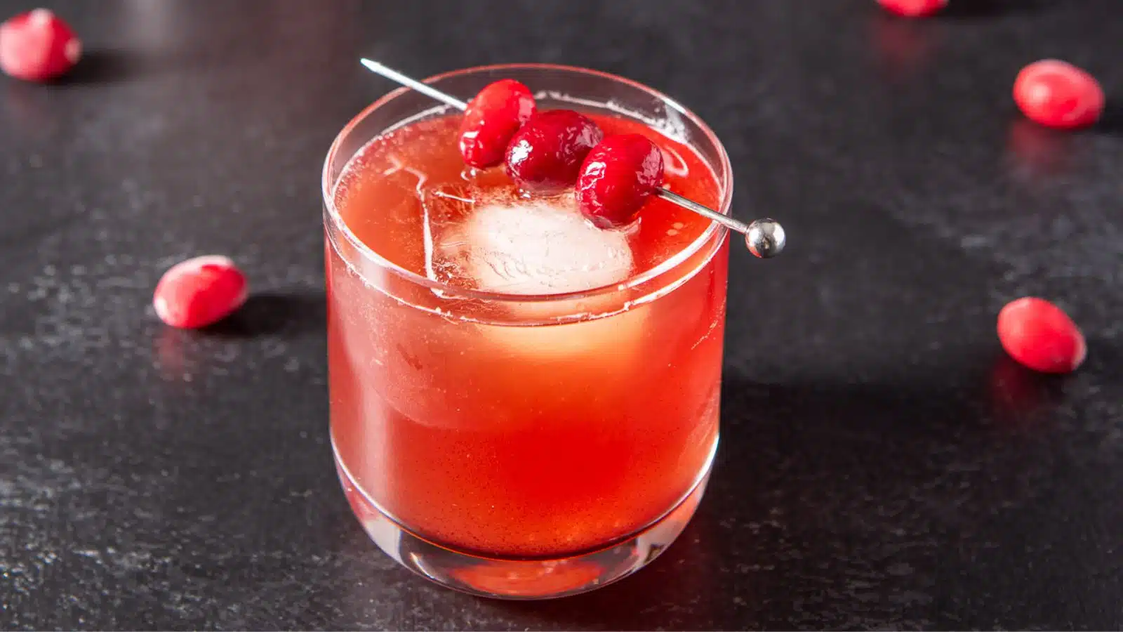 a glass with cranberries on a pick on the rim which is filled with the cranberry drink