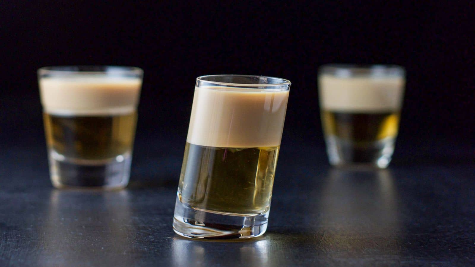 three glasses, one tilted layered with a amber liqueur and beige