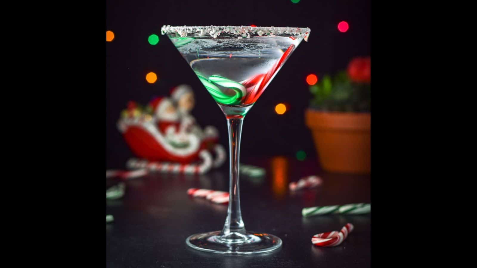 Vertical view of the clear martini with candy canes in it and lights in the back