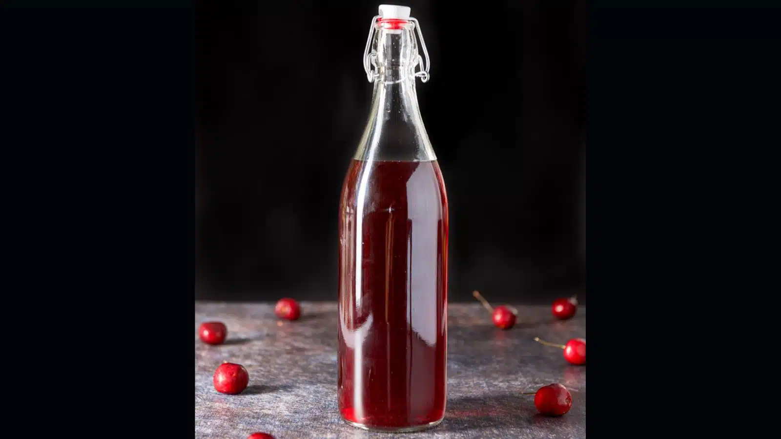 A tall glass bottle filled with cherry vodka with cherries on the table
