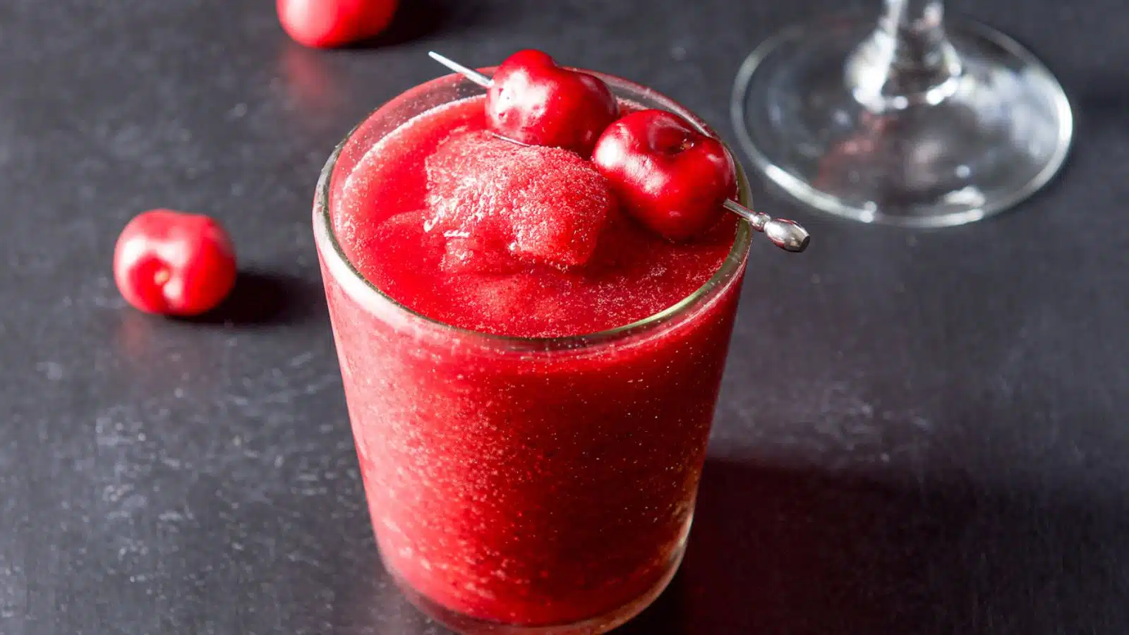 A double old fashioned glass filled with the frozen cherry margarita with cherries as garnish